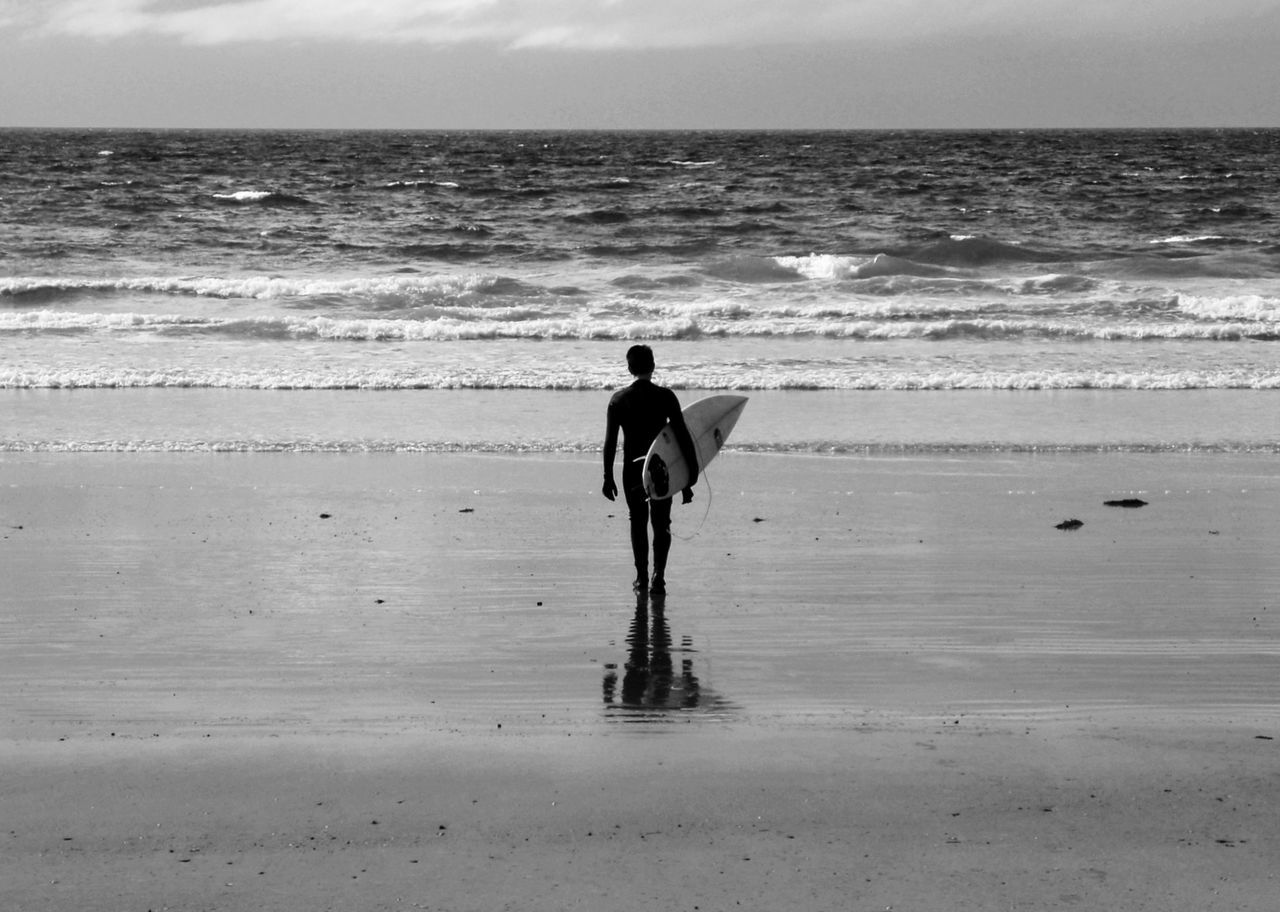 Rear view of surfer carrying surfboard on shore at beach