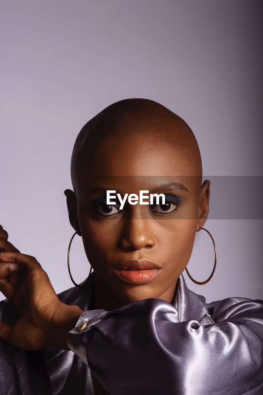 Close-up portrait of bald young woman against gray background