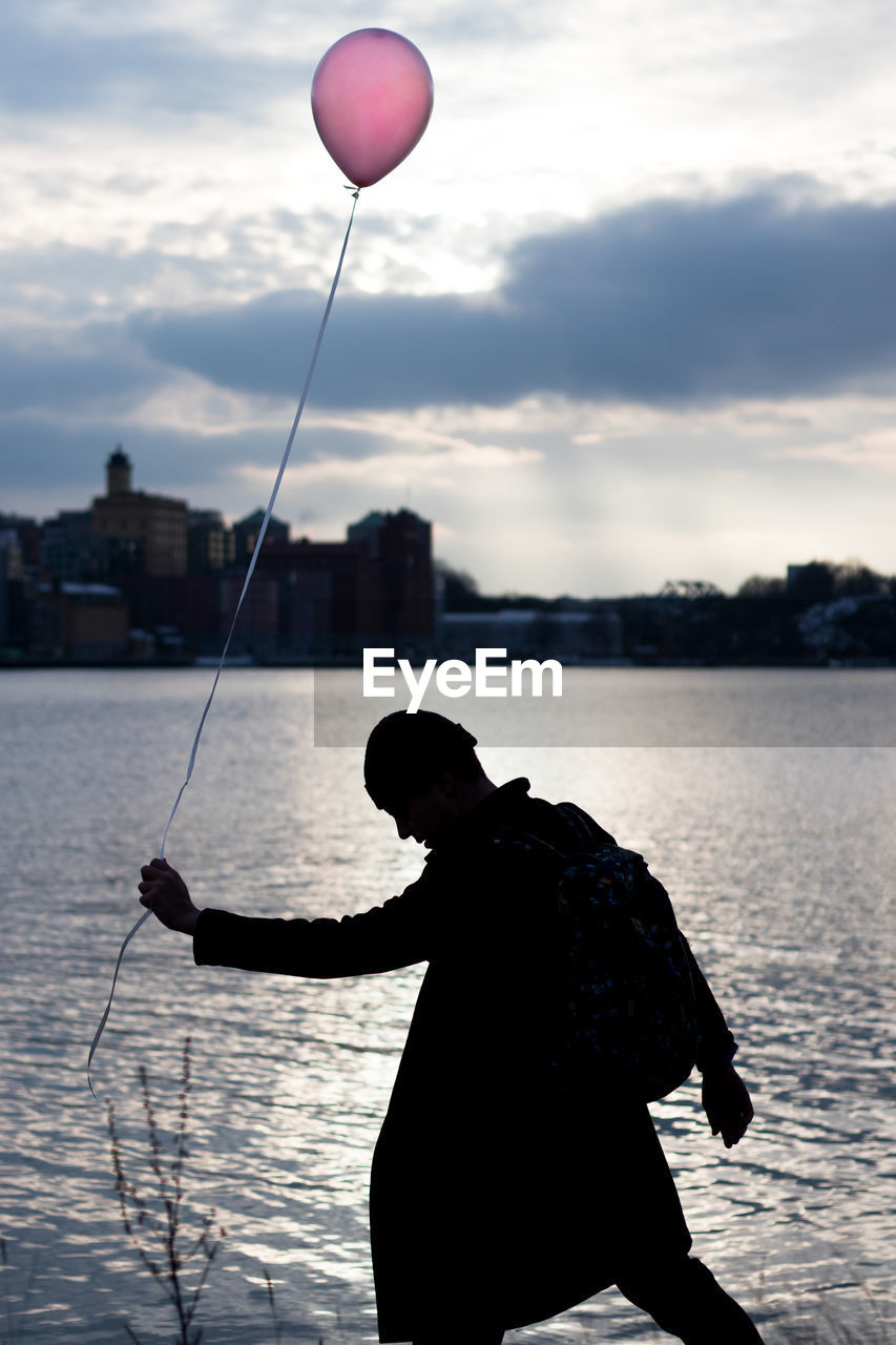 Silhouette man holding balloon by lake