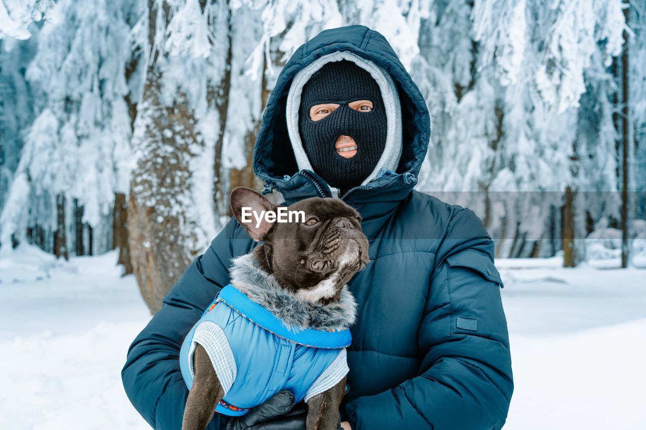 Man with ski mask and french bulldog in winter forest