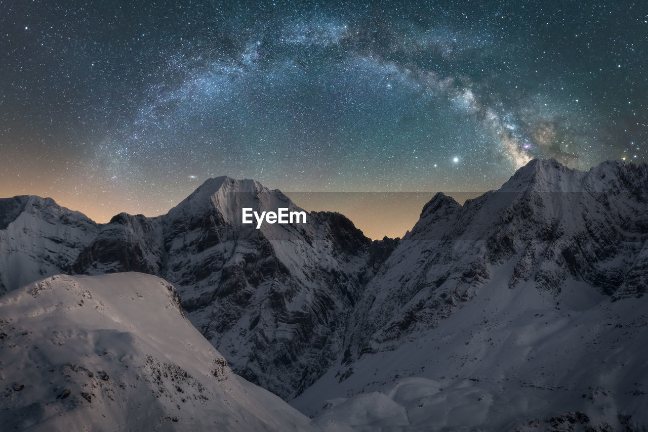 Spectacular view of high rough ridge covered with snow under colorful starry sky during milky way phenomenon