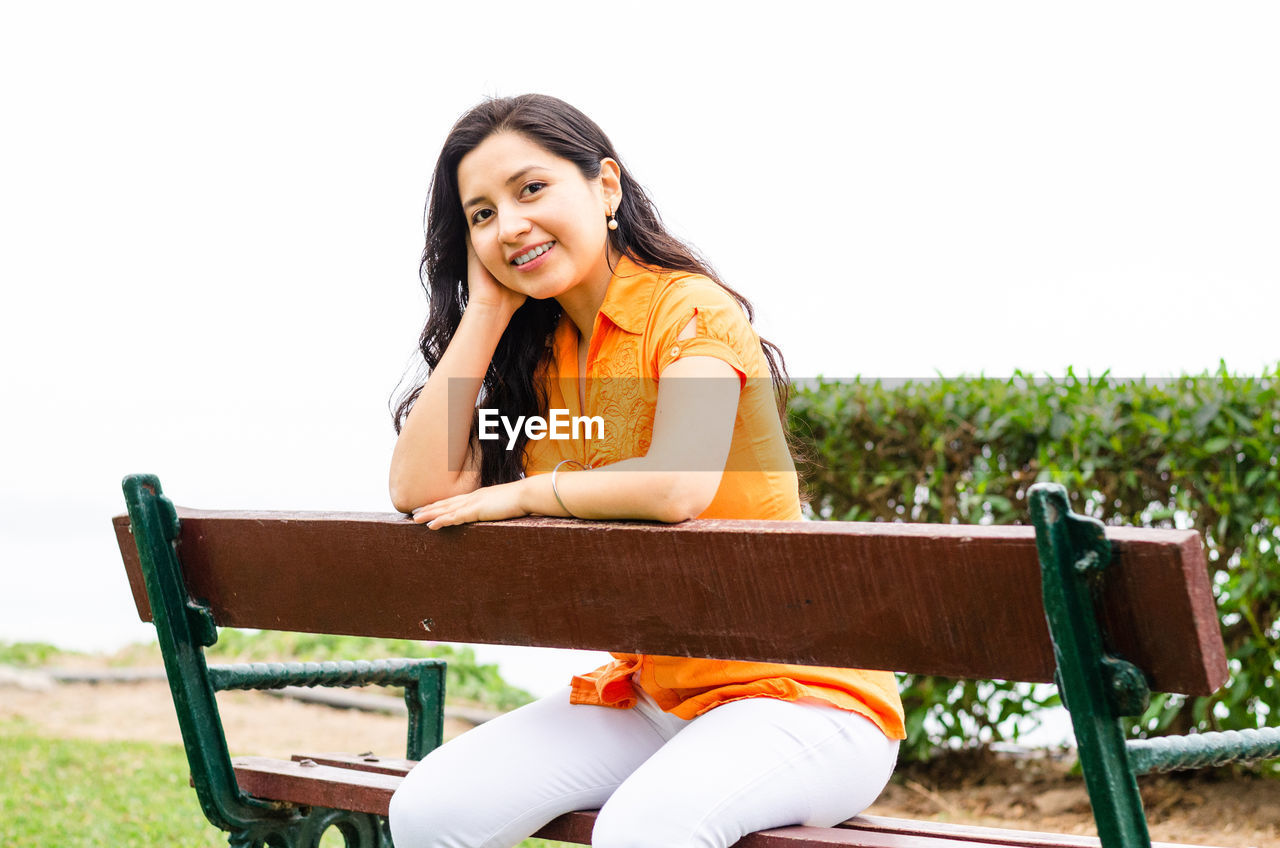 Smiling young woman sitting on chair against sky