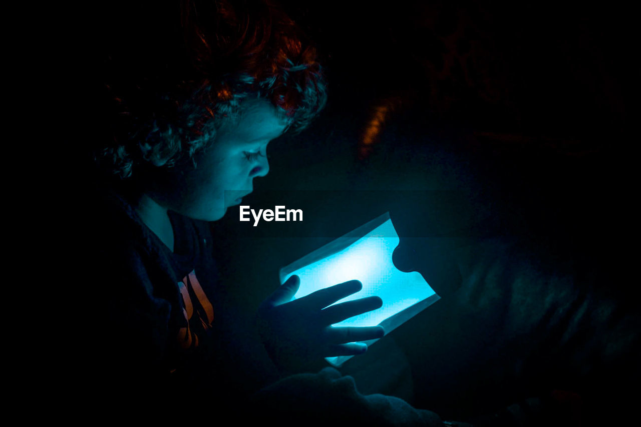 Close-up of boy holding illuminated light in darkroom