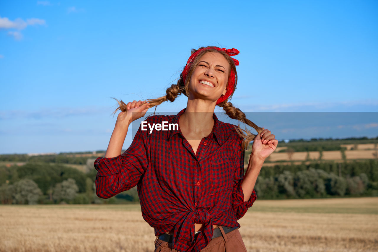 PORTRAIT OF SMILING WOMAN STANDING ON FIELD