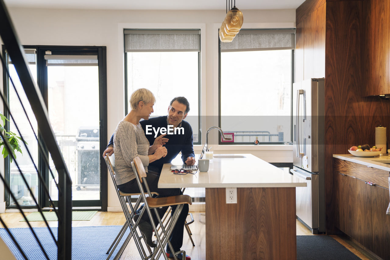 Senior couple discussing while sitting by laptop computer at home