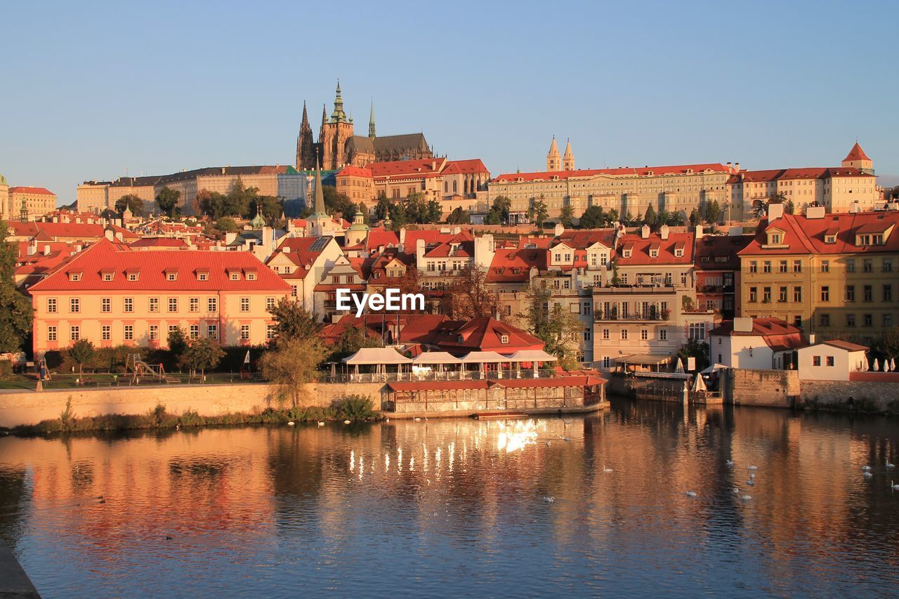 Buildings in city against clear sky and reflecting on the river 