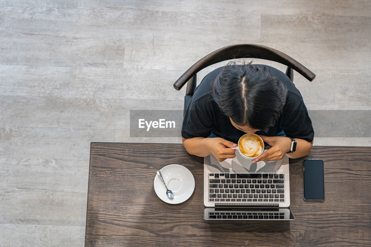 Overhead view photo of woman enjoying latte and using laptop