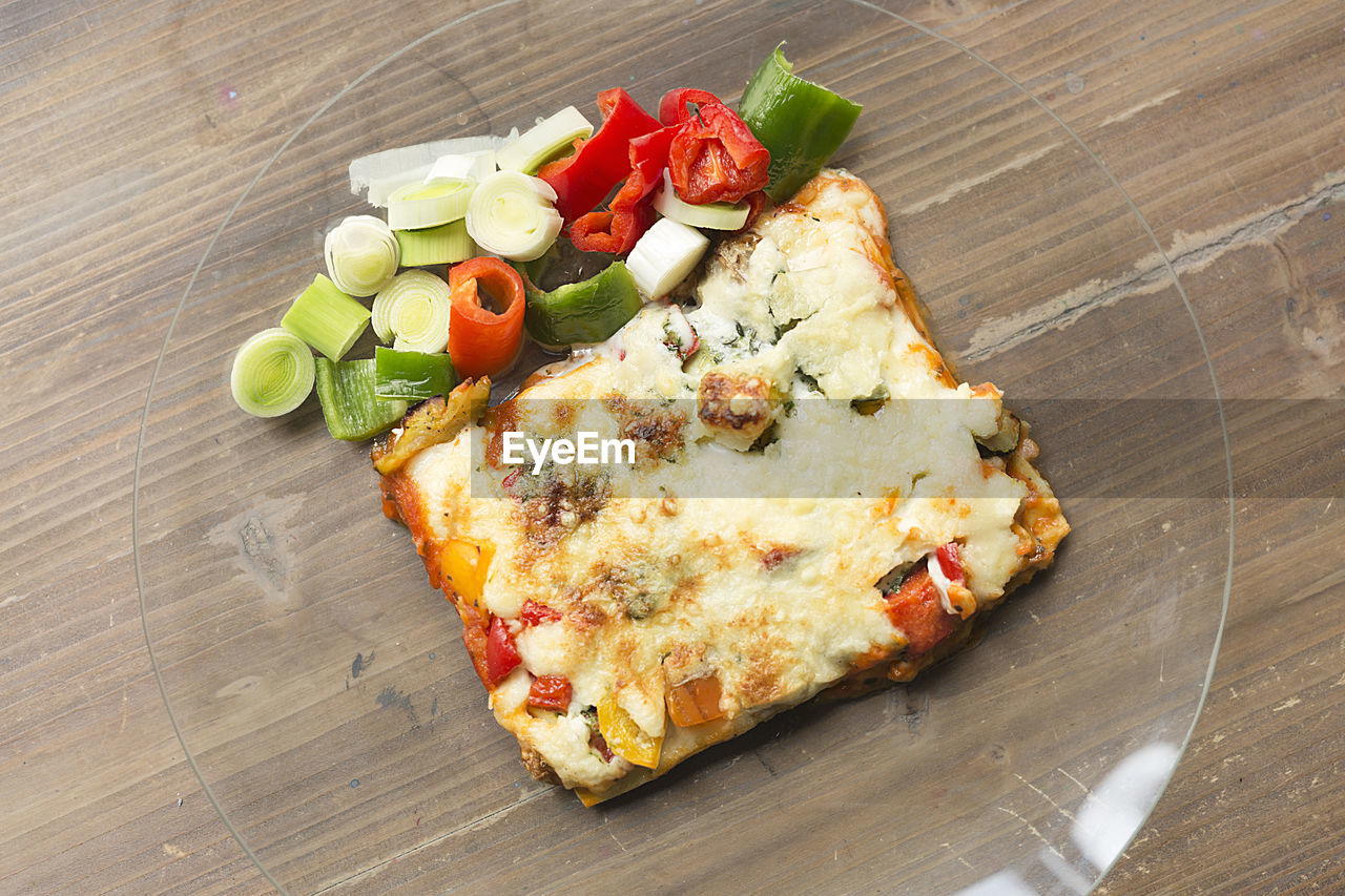 Italian food known as lasagna on a glass plate and a wooden background.