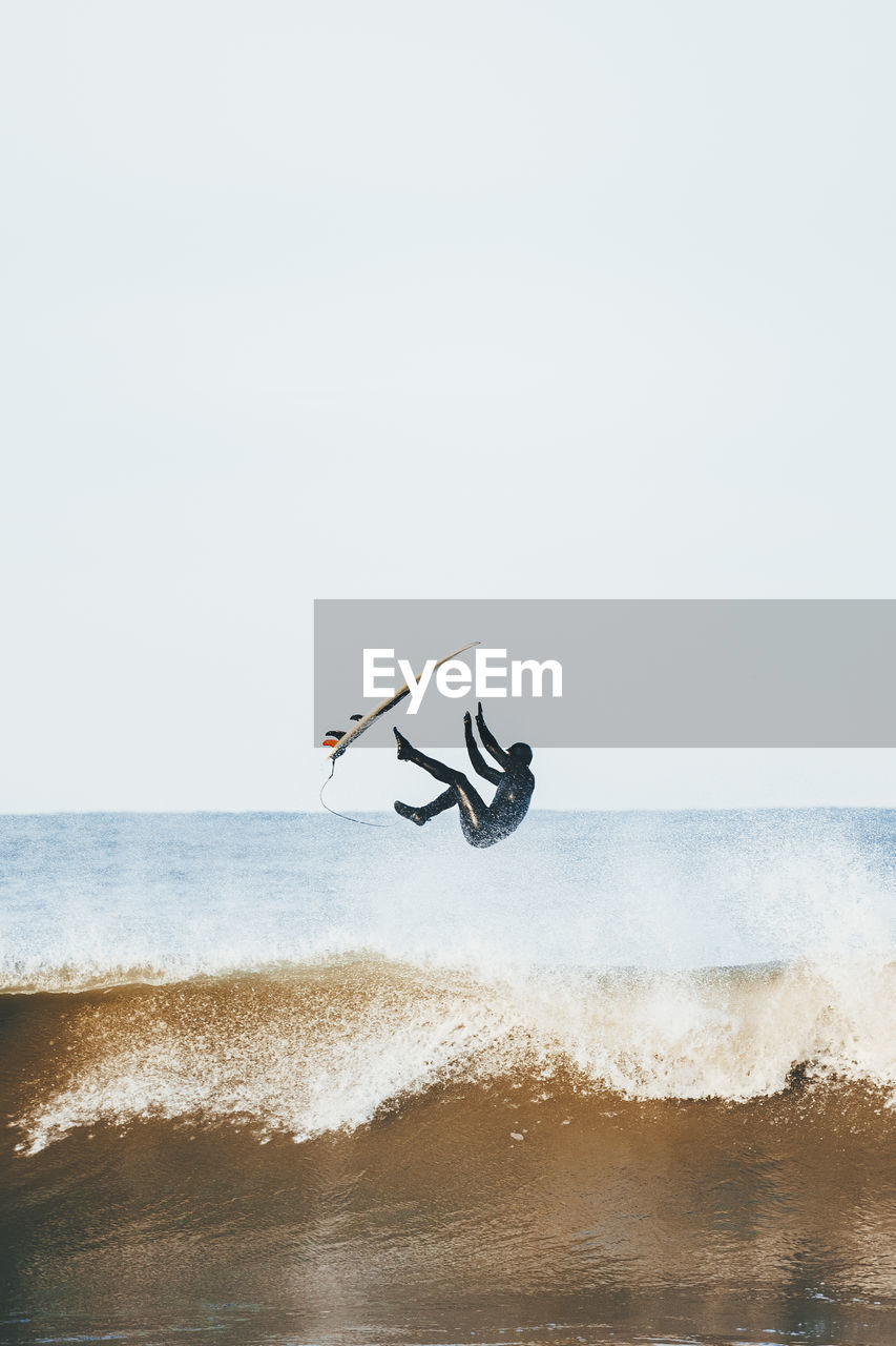 Man with surfboard jumping over sea on sunny day