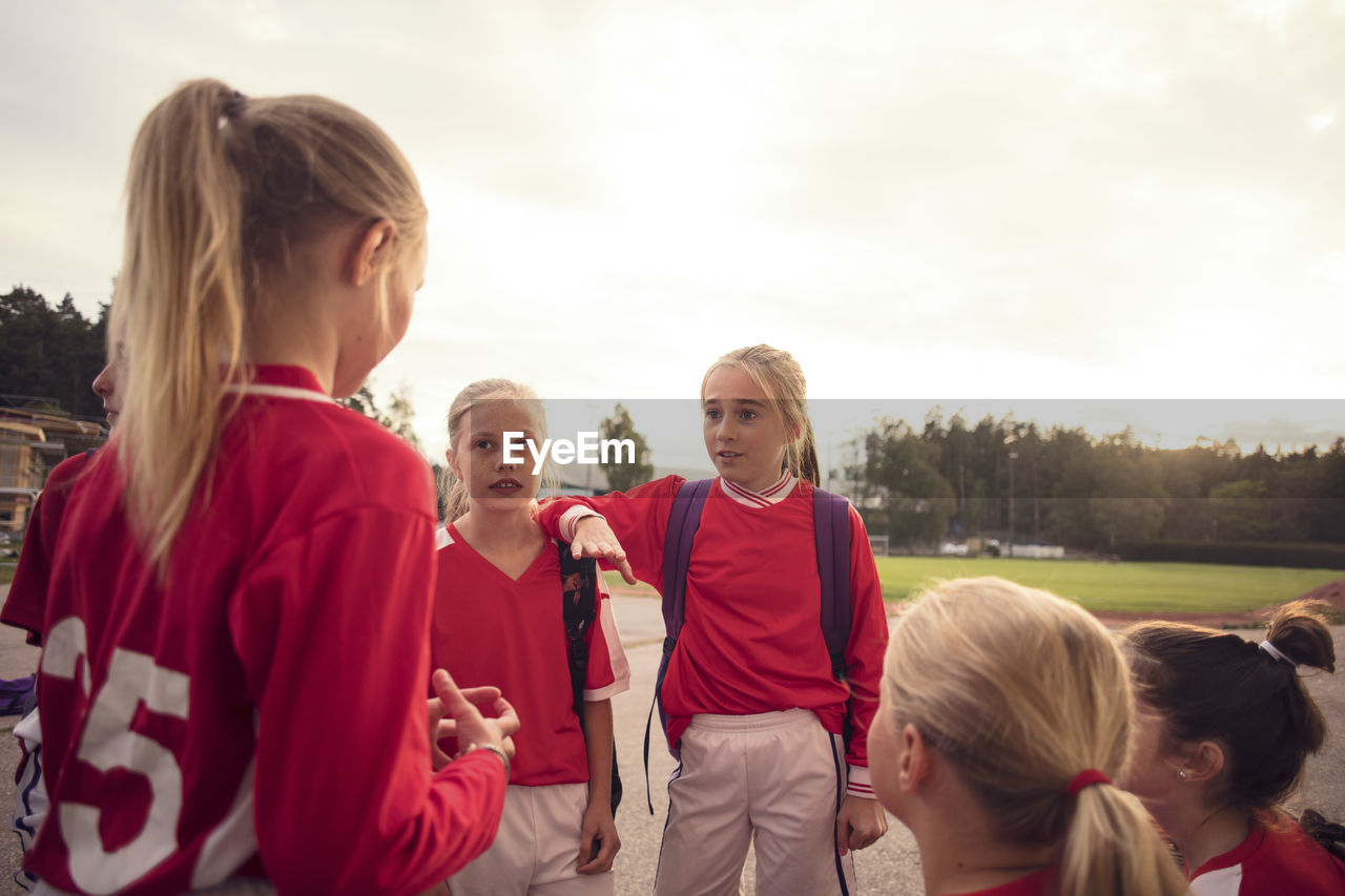 Girls wearing red soccer uniform talking against sky