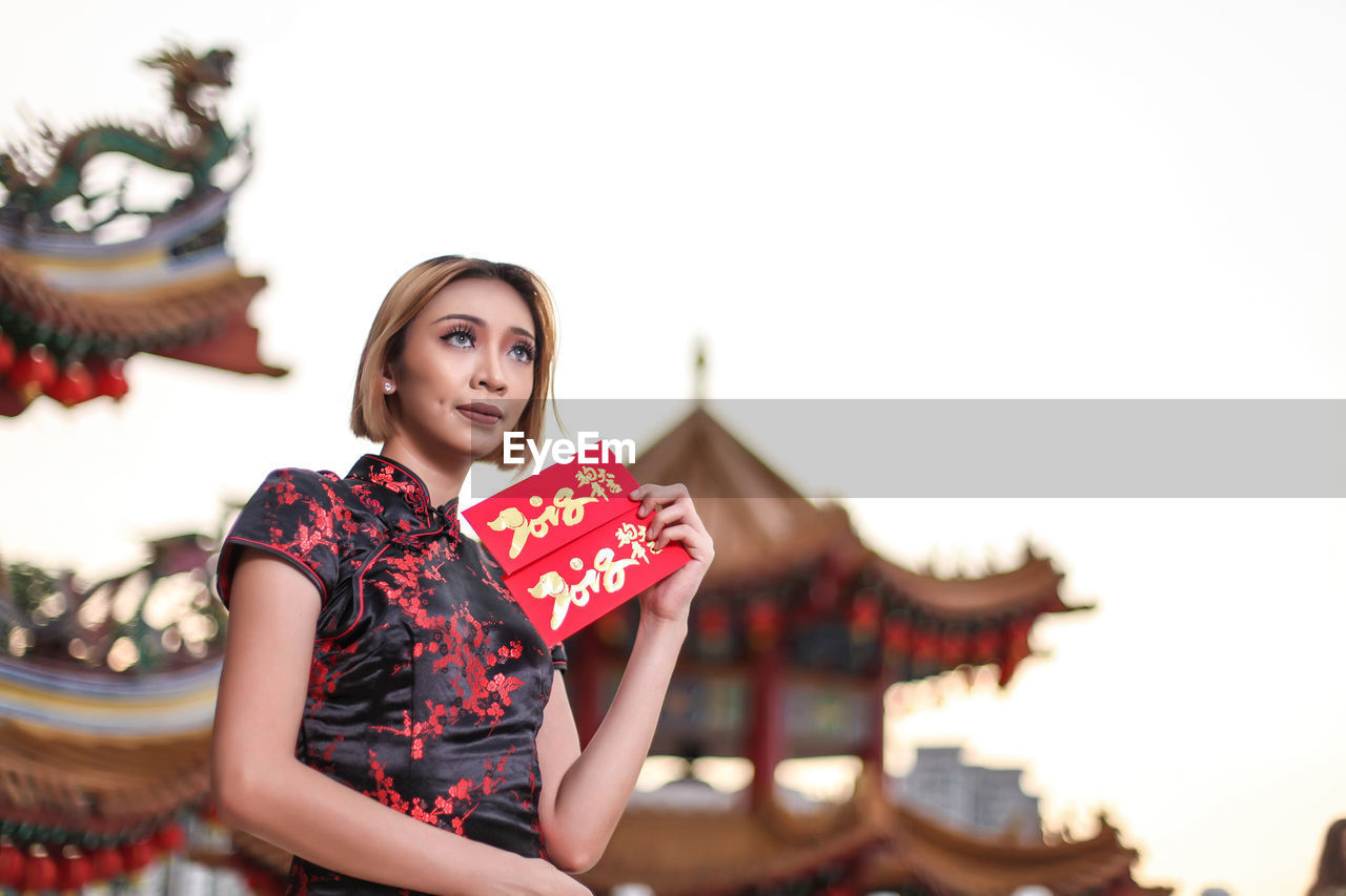 Low angle view of woman holding envelope against clear sky