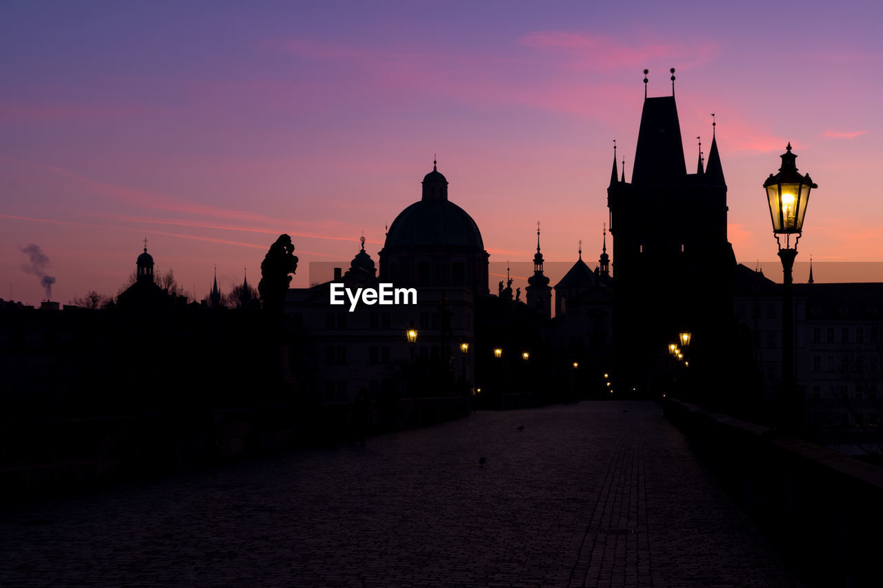 Silhouette of towers of old town in prague, view from illuminated charles bridge during sunrise