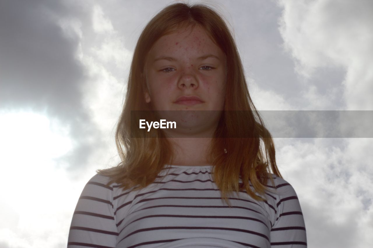 Low angle portrait of girl standing against cloudy sky