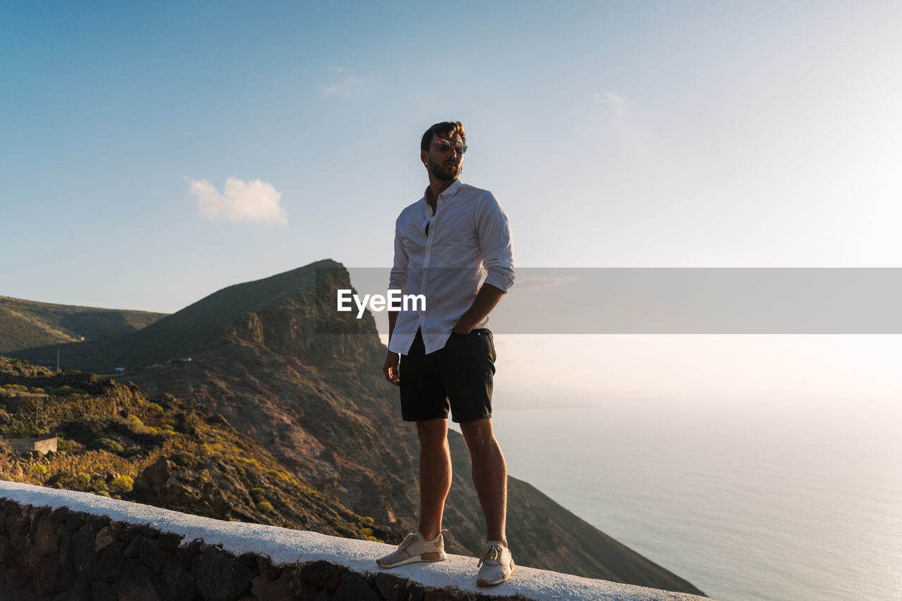 Full length of man standing on retaining wall against sky