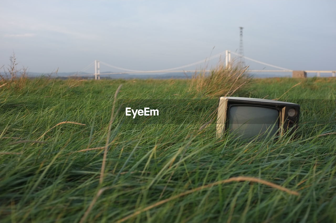 Abandoned television set on grassy field against sky