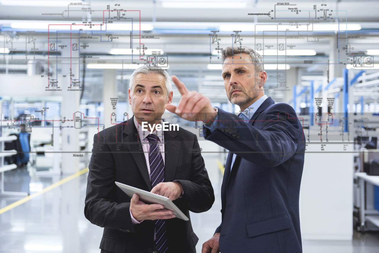 Two businessmen looking at graphic on glass pane in factory hall