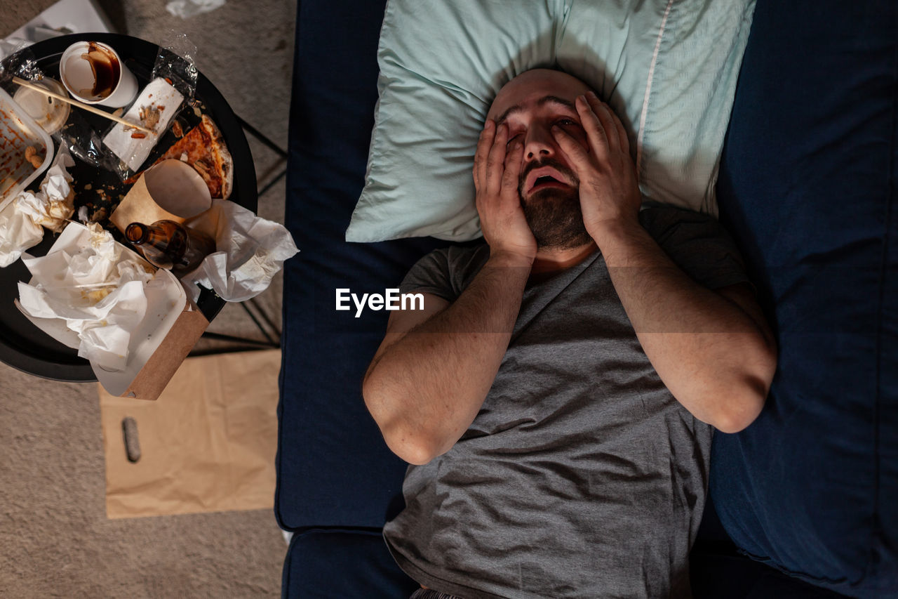 Depressed frustrated man in despair laying on couch, feeling irritated about solitude and loneliness