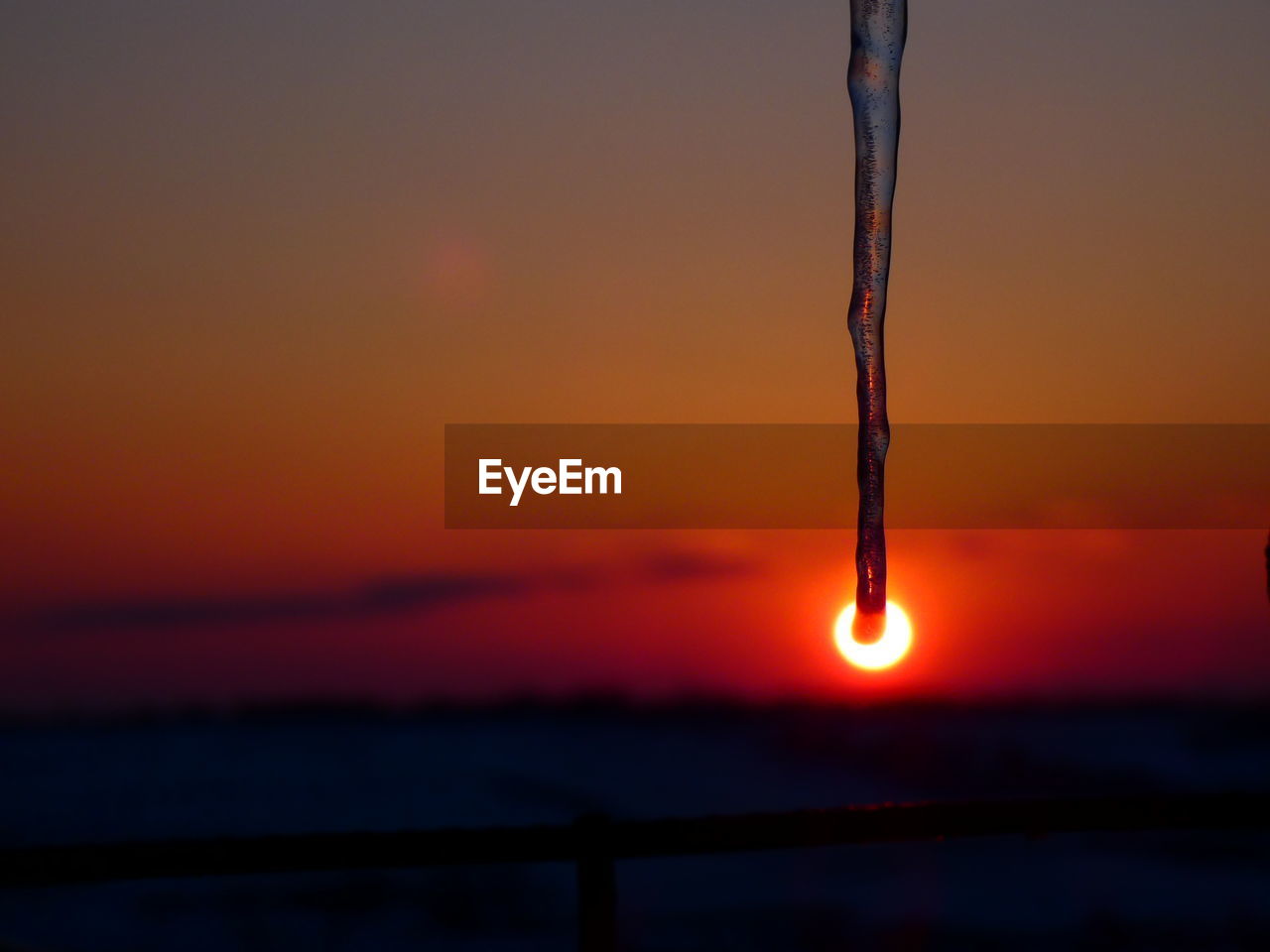 CLOSE-UP OF ICICLES AGAINST ORANGE SUNSET SKY