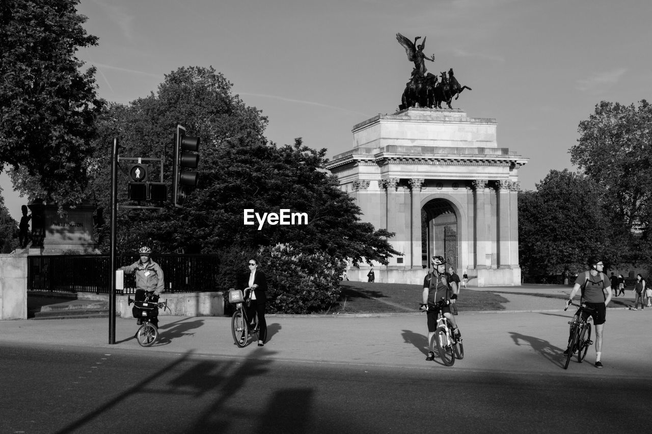 People with bicycles on street against wellington arch in city