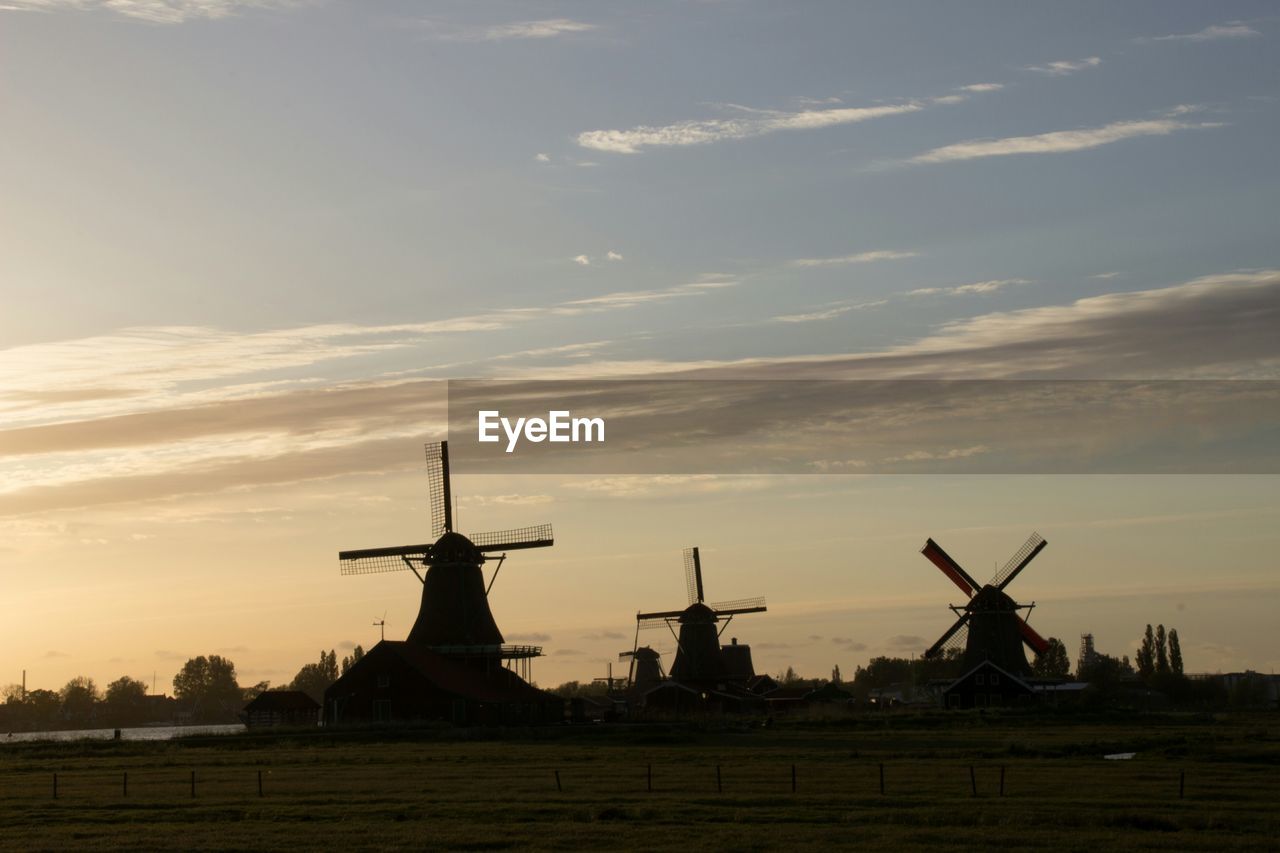 Traditional windmills on field against sky during sunset