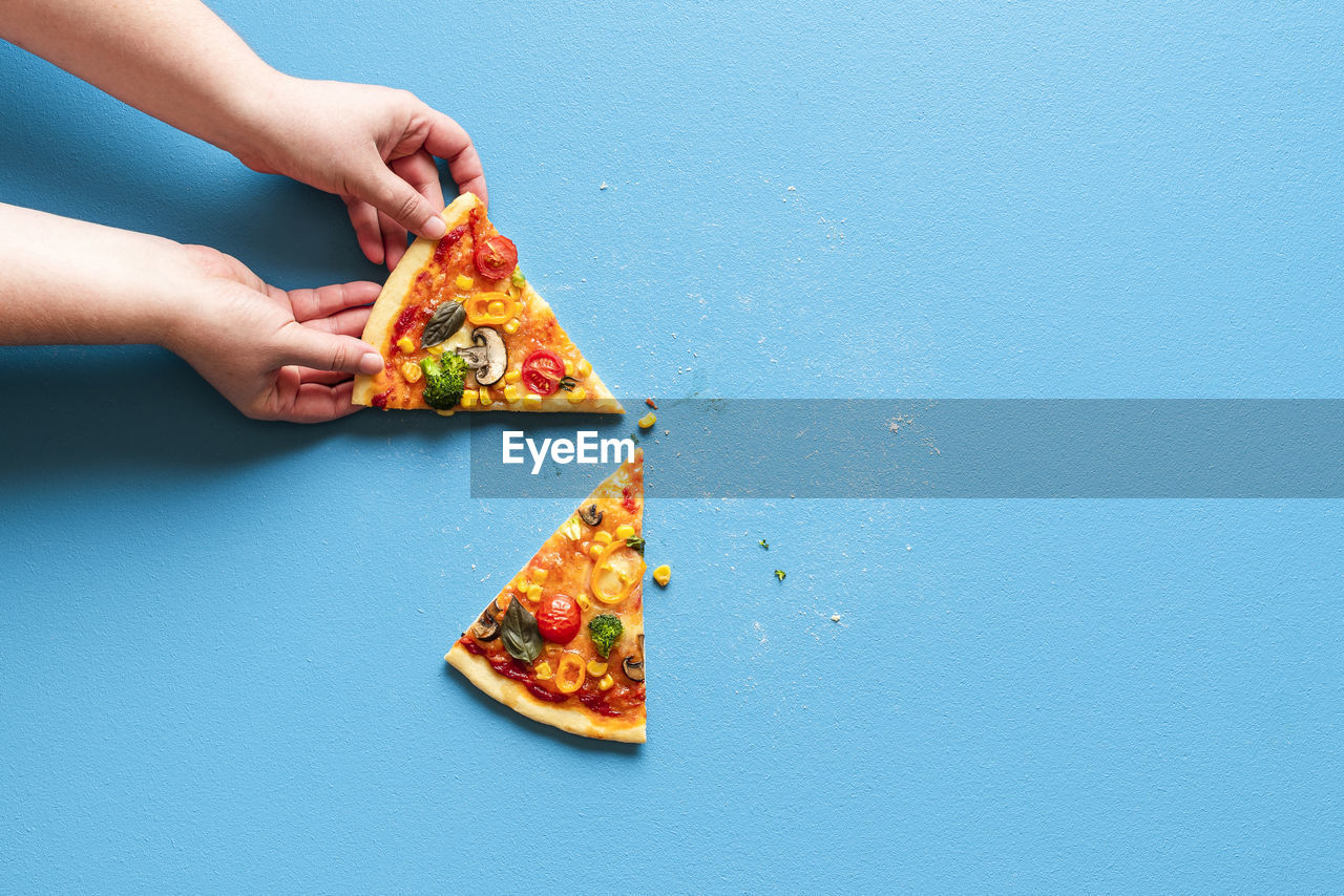 Woman's hand grabbing a slice of vegetarian pizza. slices of pizza primavera on a blue table.