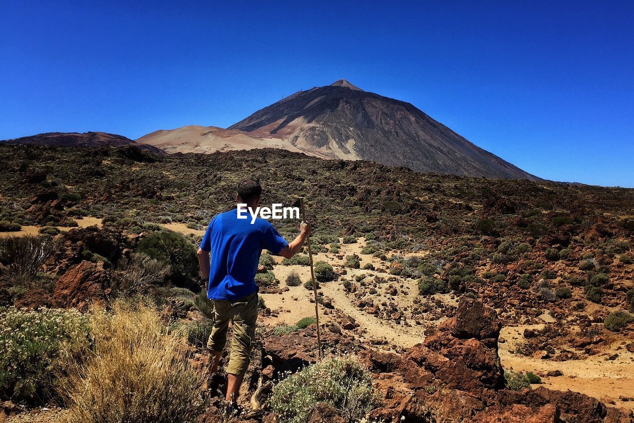 Rear view of man climbing on mountain against clear sky