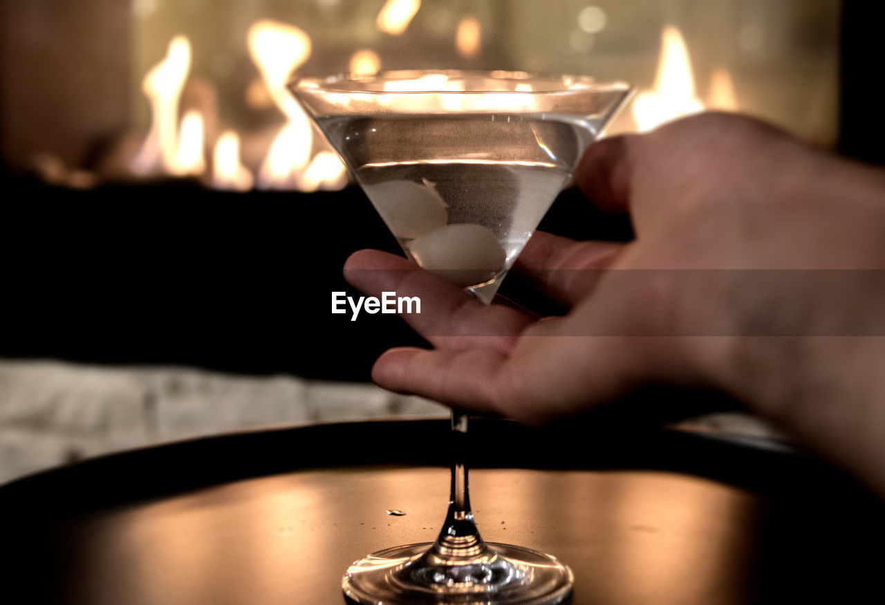 Cropped image of hand holding martini glass on tray against fireplace