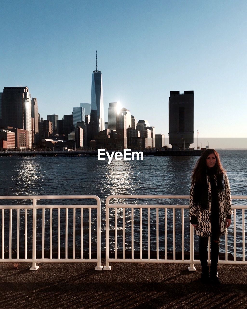 Woman standing at railing against river and city