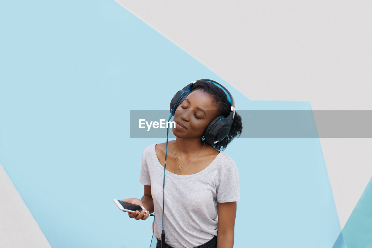 Young woman listening music against colored background