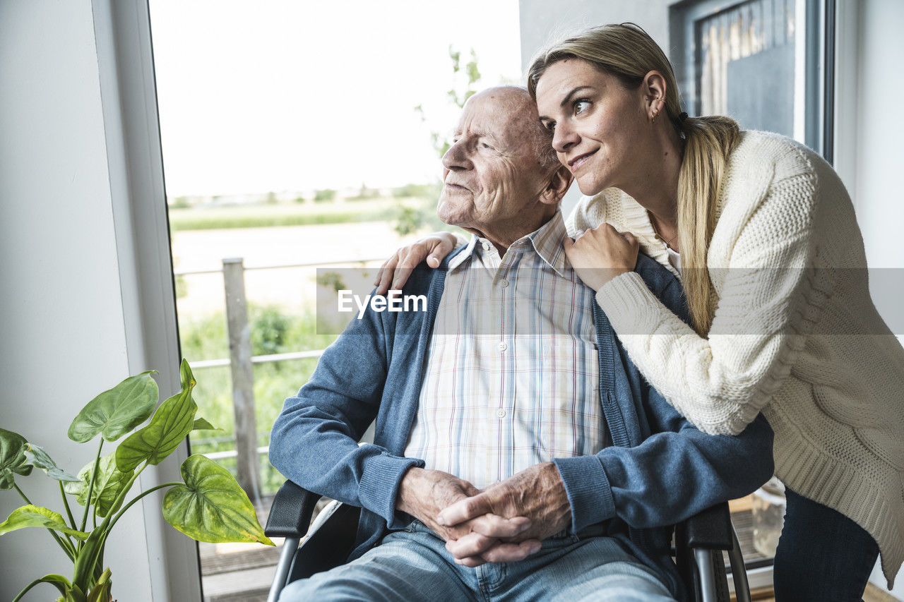 Smiling blond woman taking care of father sitting in wheelchair at home
