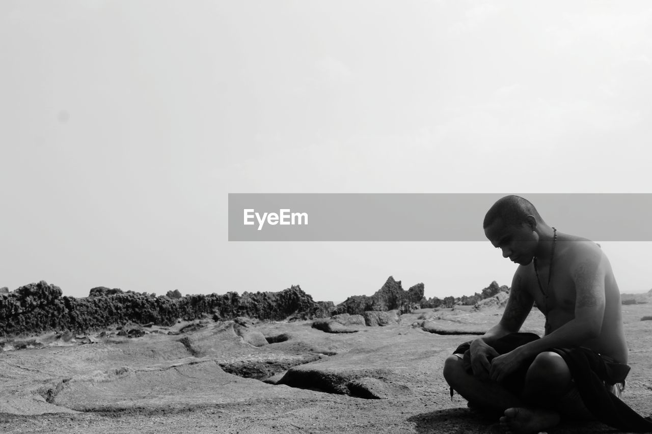 FULL LENGTH OF MAN SITTING ON ROCK