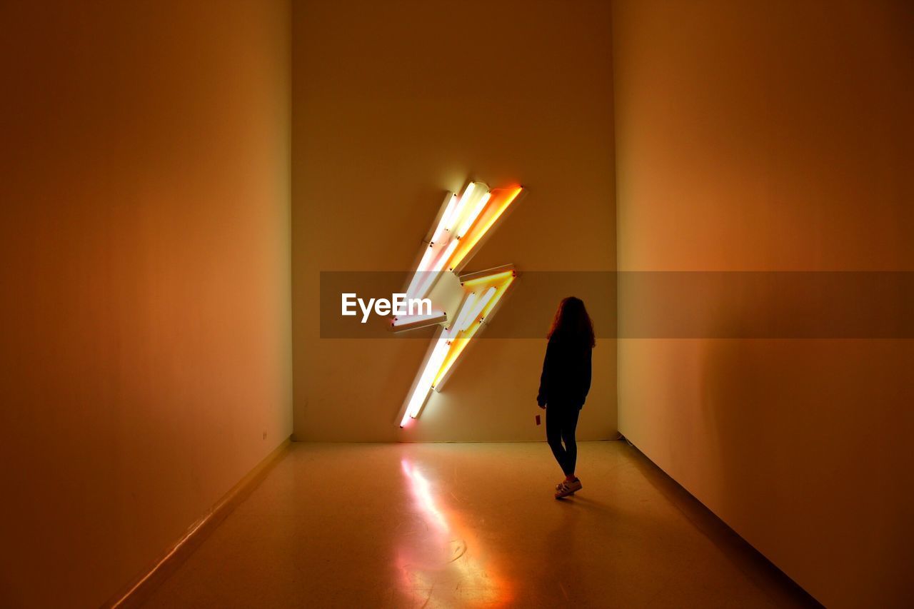 Silhouette woman standing against illuminated sign in room