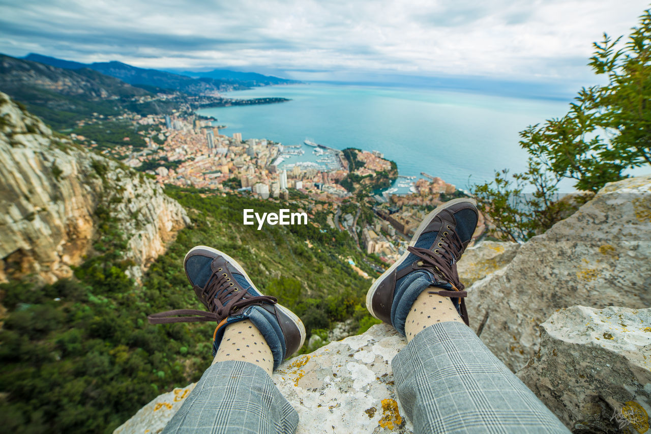 Low section of man sitting on mountain against landscape