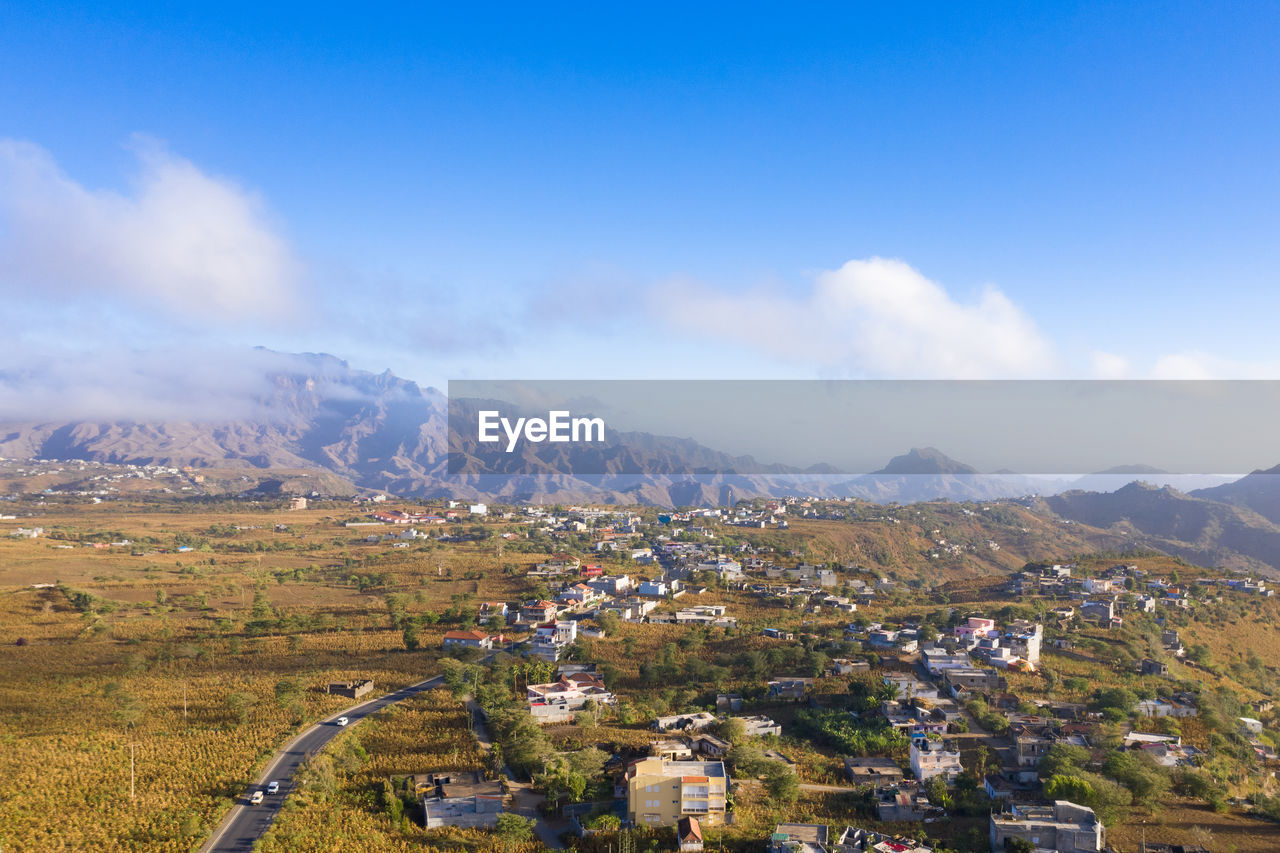 AERIAL VIEW OF TOWNSCAPE BY MOUNTAINS AGAINST SKY