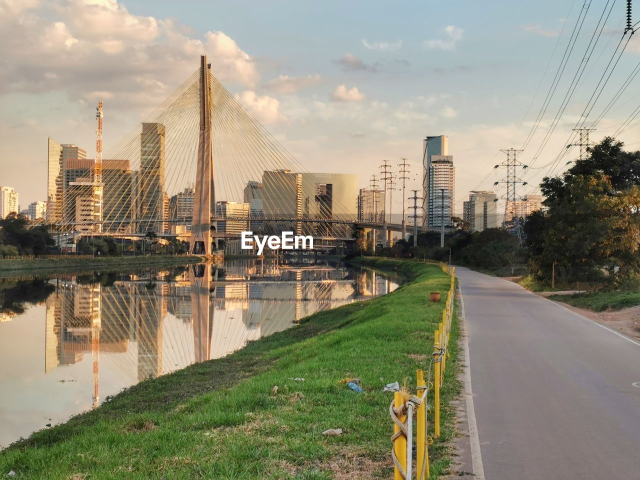 ROAD BY RIVER AMIDST BUILDINGS AGAINST SKY