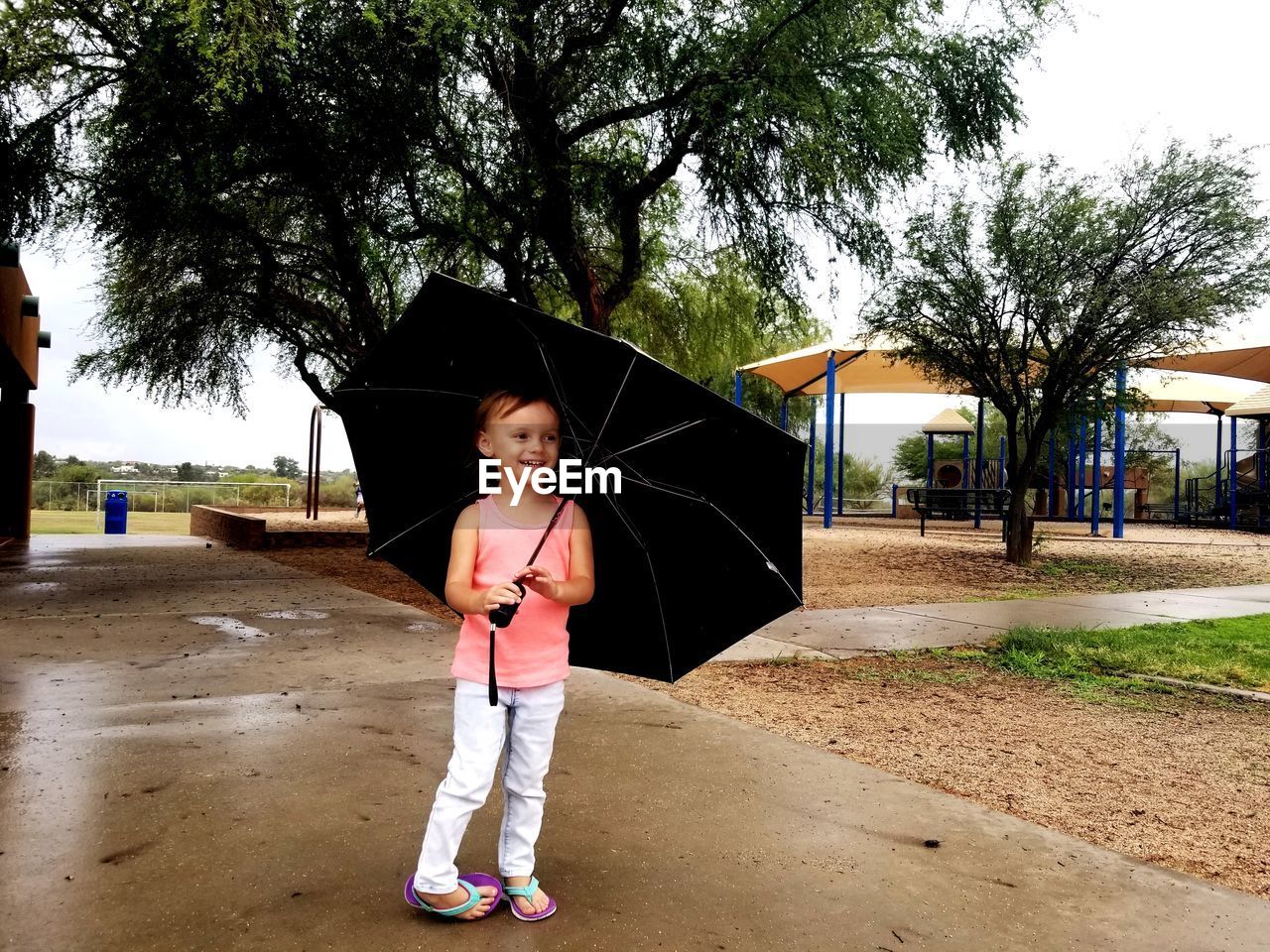 Full length of cute girl holding umbrella while standing on footpath