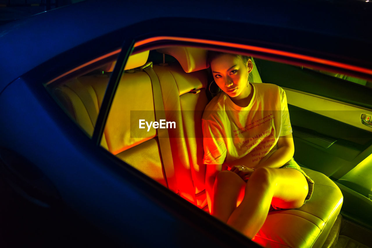 YOUNG WOMAN LOOKING AWAY WHILE SITTING ON CAR