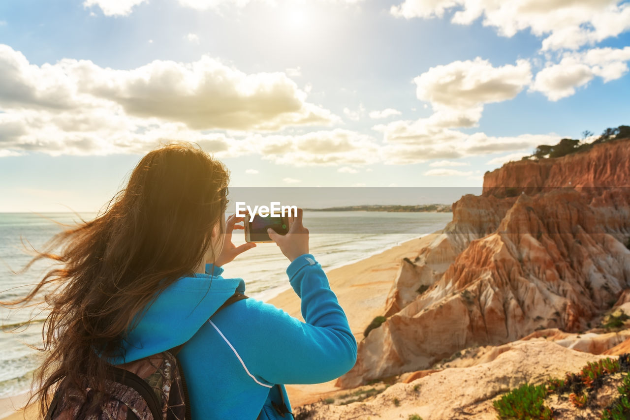 Rear view of woman photographing at beach against sky