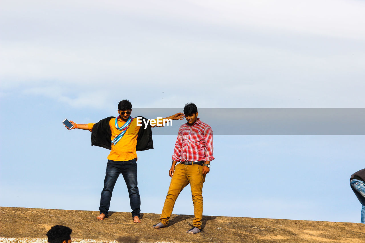 Young friends standing on concrete wall against sky