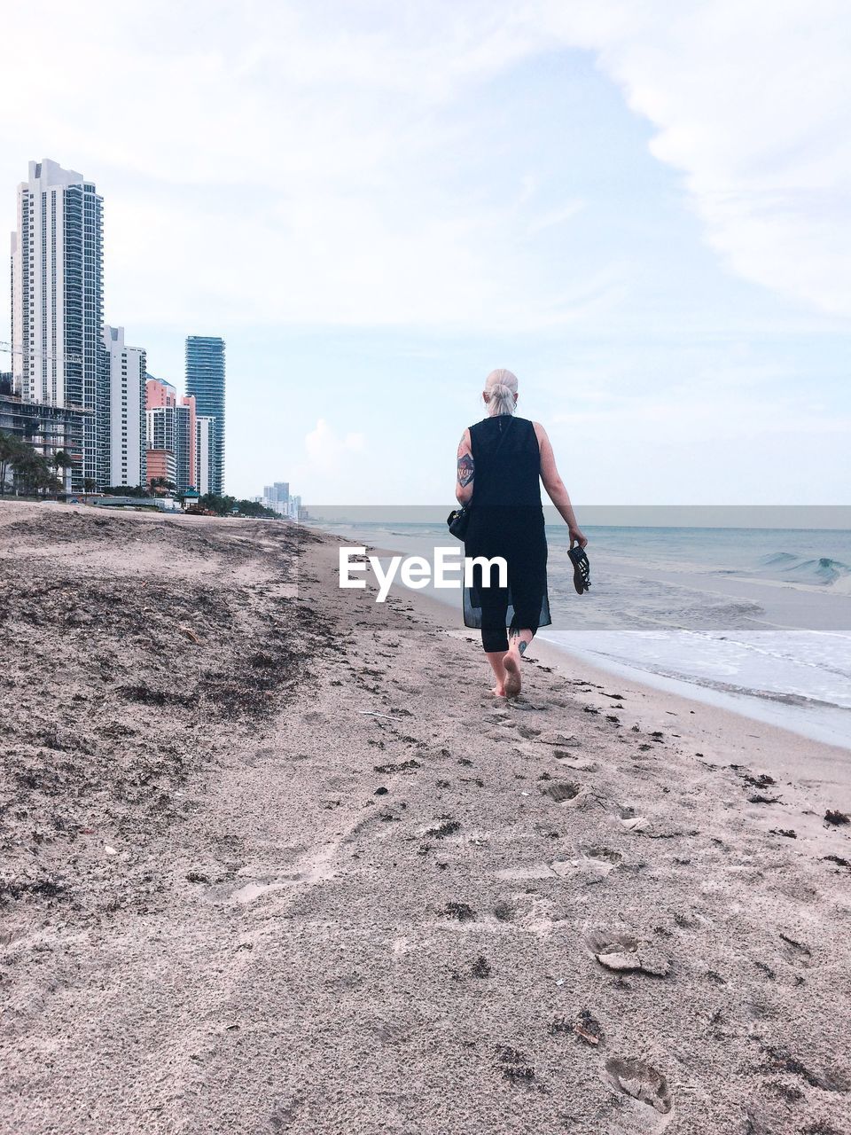 Rear view of woman walking at beach against sky in city