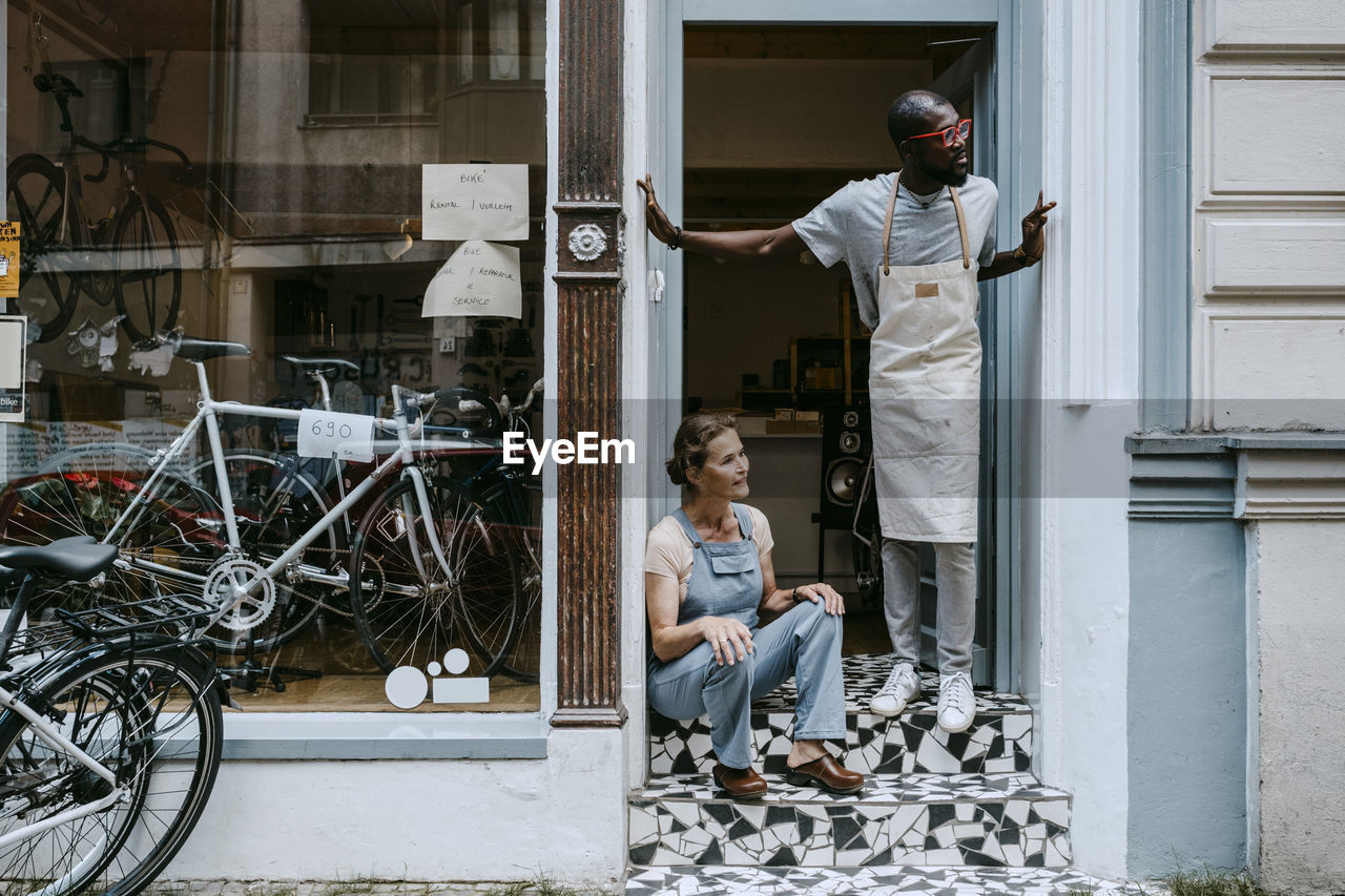 Senior owner and colleague looking away against bicycle shop