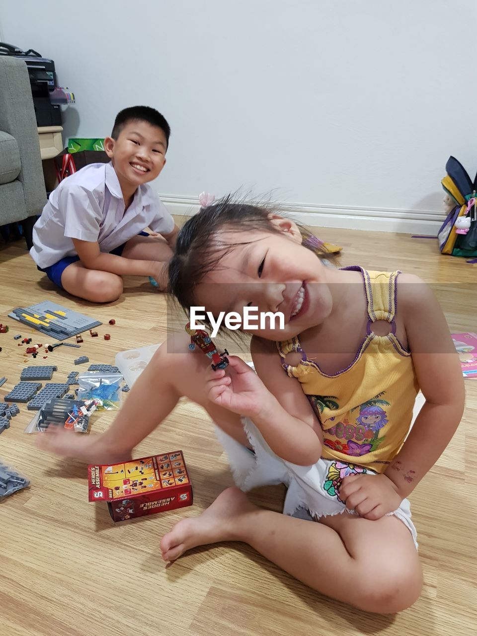 Portrait of smiling siblings playing with toy while sitting on floor at home