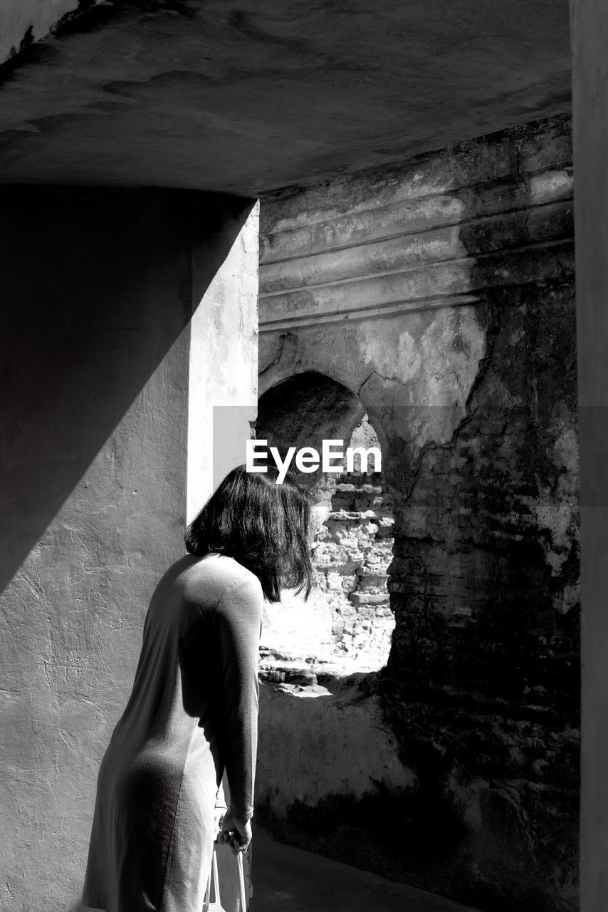 Side view of woman looking through window at abandoned building