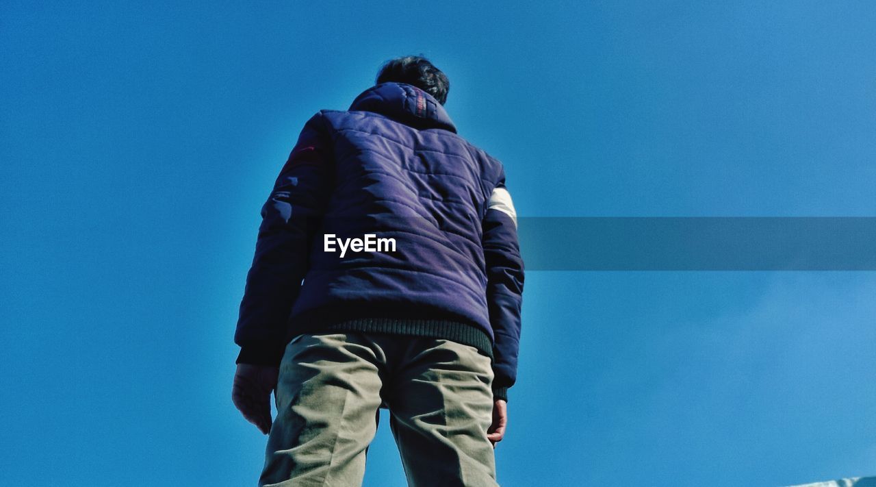 LOW ANGLE VIEW OF MAN WITH BLUE UMBRELLA AGAINST CLEAR SKY