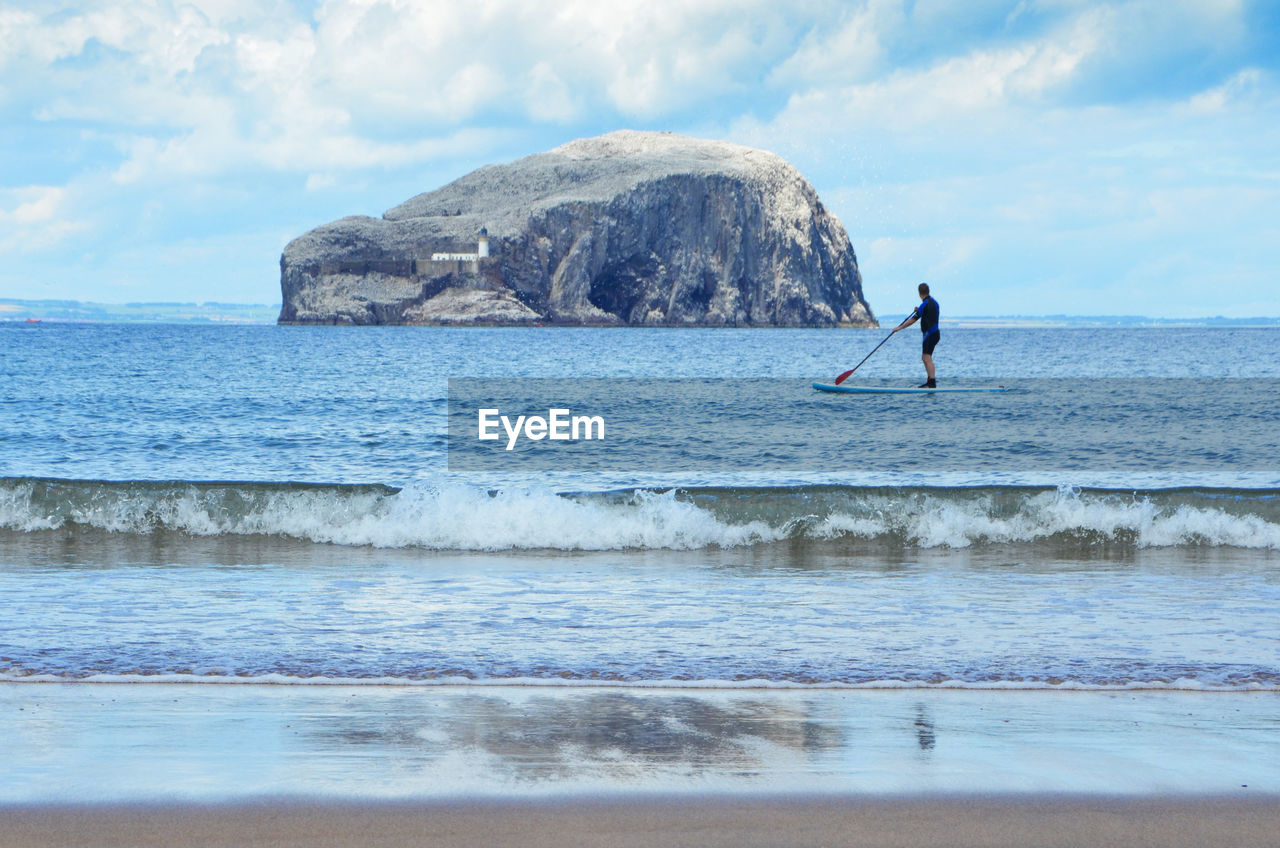 Man paddleboarding on sea against sky