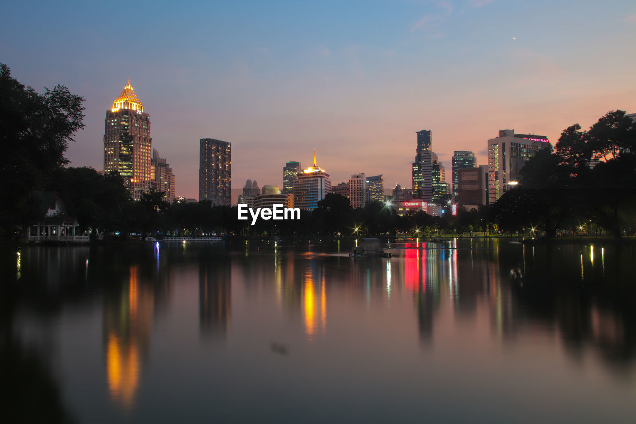 Illuminated buildings by river against sky in city