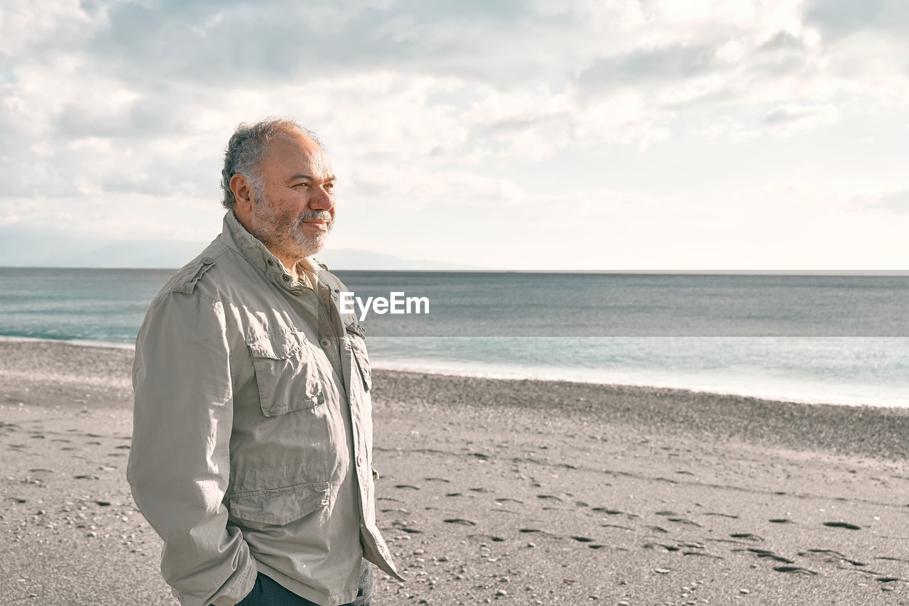 Happy middle-aged bearded man walking along deserted winter beach.
