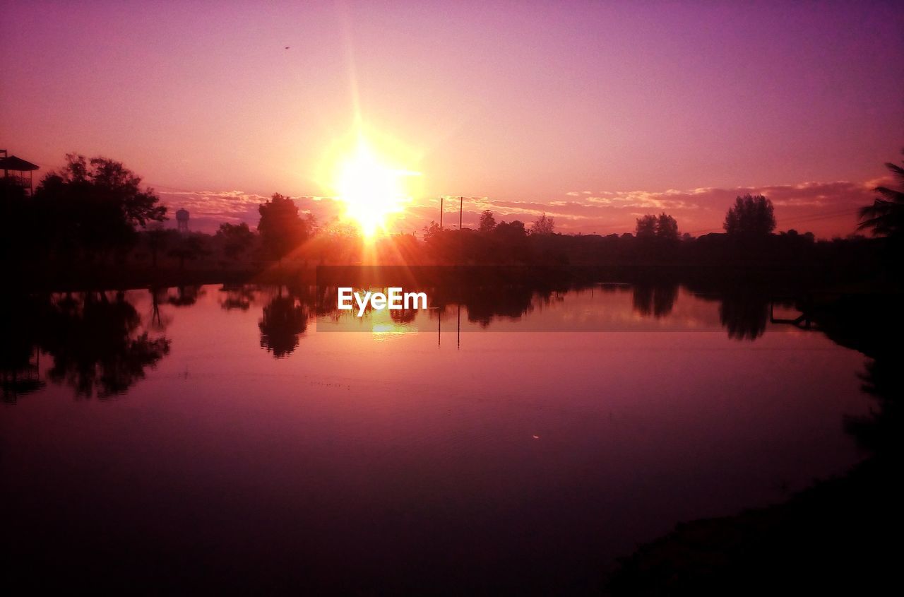 REFLECTION OF SILHOUETTE TREES ON LAKE AGAINST SKY DURING SUNSET