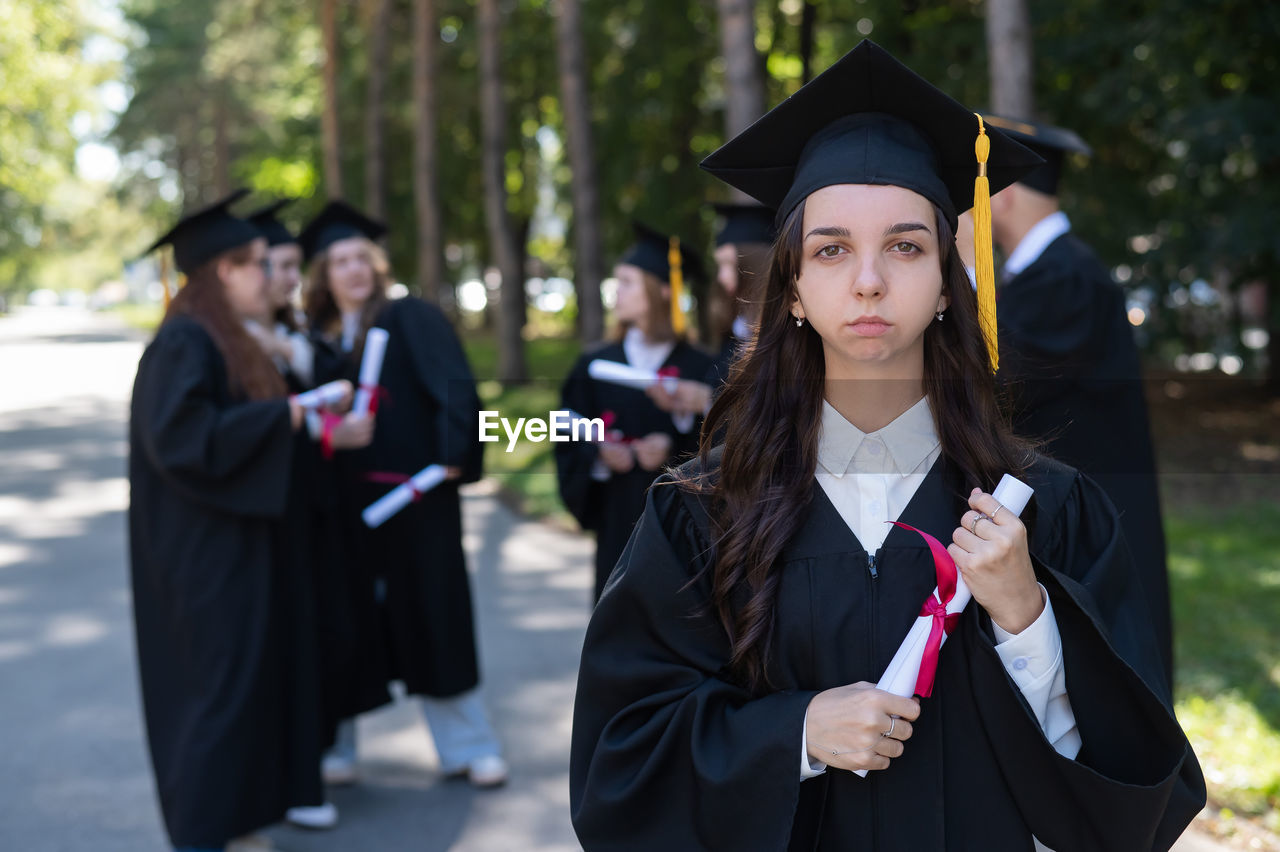 portrait of smiling young woman wearing graduation gown standing on street