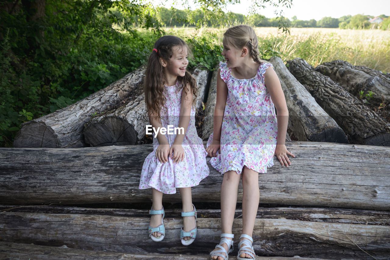 Full length of smiling sisters sitting on log